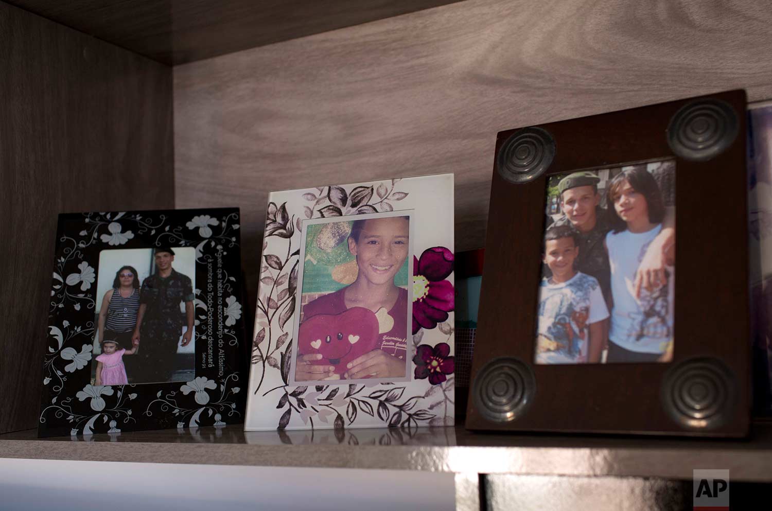 In this Aug. 13, 2017 photo, family portraits of Felipe Farias line a shelf in his mother's new apartment, in the Alemao complex of slums, in Rio de Janeiro, Brazil. The 16-year-old was killed on April 26 in the Alemao while returning from a protest condemning the death of a 13-year-old who was also killed by gunfire. (AP Photo/Silvia Izquierdo)