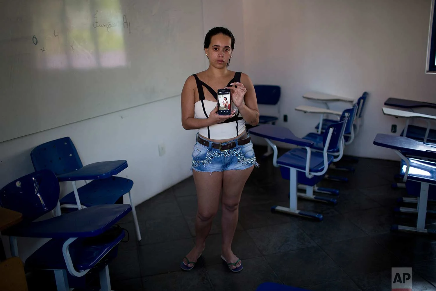 In this Sept. 6, 2017 photo Thayana Caparica poses with a photo of her 7-year-old daughter Fernanda, at the Mare complex of slums, in Rio de Janeiro, Brazil. Classes at Fernanda's school were canceled on the morning of Feb. 15, due to gunfire between gangs. Caparica took her daughter home and ordered Fernanda and her two brothers not to leave the house. But by the afternoon Fernanda had grown impatient and wanted to play outside. She kept insisting. Finally Caparica let her go to a friend's house. Later that day she learned that her daughter had been shot in the face. (AP Photo/Silvia Izquierdo)