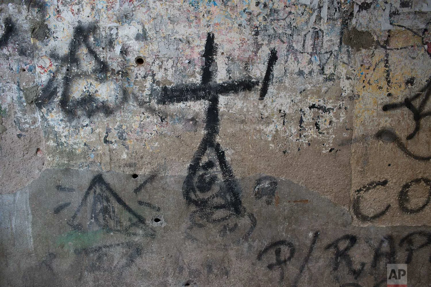 This Aug. 13, 2017 photo shows a cross scrawled on the wall pockmarked with bullet holes of the narrow alley where 16-year-old Felipe Farias died, in the Alemao complex of slums, in Rio de Janeiro, Brazil. Several witnesses have testified that the fatal shot came from police. However, investigators have told Felipe's mother they will not go to the crime scene for fear of being attacked by a local gang. (AP Photo/Silvia Izquierdo)