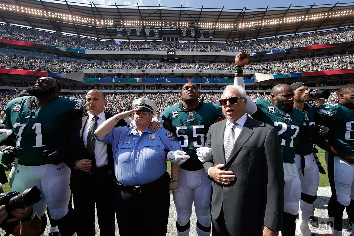 Philadelphia Eagles players, owner Jeffrey Lurie, center right, Eagles' President Don Smolenski, second from left, and a Philadelphia police officer, third from left, stand for the national anthem before an NFL football game against the New York Gia
