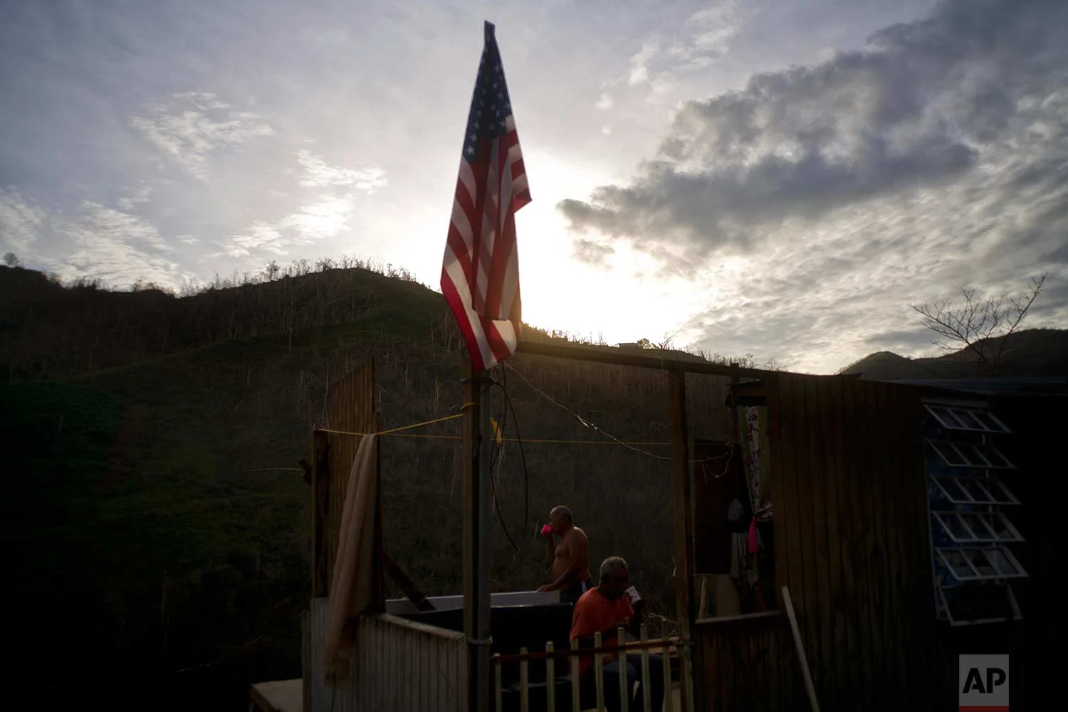 Ramon Sortre Vazquez, back, drinks coffee next to his brother Angel Luis, next to a flag of the United States in what is left of his house destroyed by Hurricane Maria, in Morovis, Puerto Rico, Sunday, Oct. 1, 2017. (AP Photo/Ramon Espinosa)