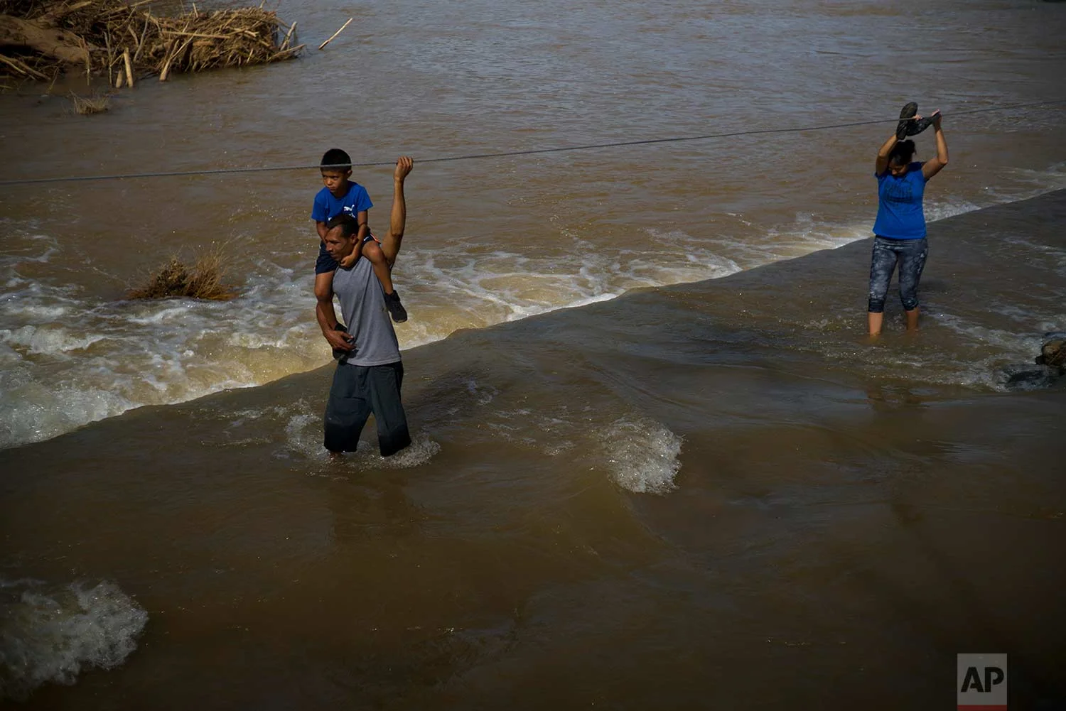 A man carries his son on his shoulders as he wades between a river in the San Lorenzo neighborhood of Morovis, Puerto Rico, Sunday, Oct. 1, 2017. (AP Photo/Ramon Espinosa)