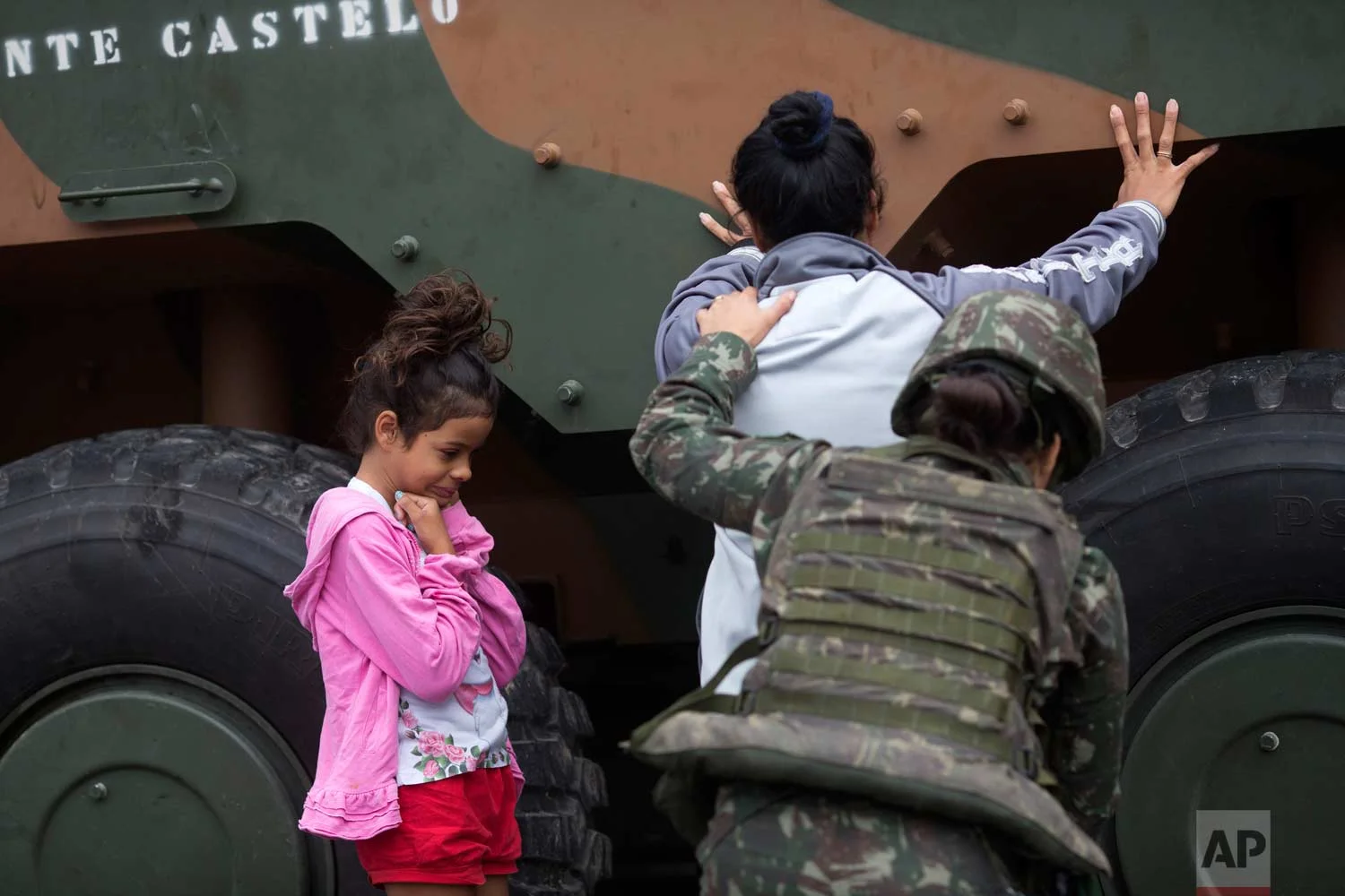 In this Aug. 21, 2017 photo, a soldier pats down a woman as a girl waits during a security operation at the Jacarezinho slum, in Rio de Janeiro, Brazil. In July the federal government deployed over 8,500 troops to try to stamp out crime in Rio's roughest neighborhoods. But so far they have not been able to stem the bloodshed. (AP Photo/Silvia Izquierdo)