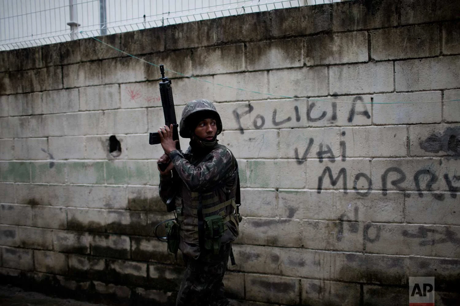 In this Aug. 21, 2017 photo, a soldier takes position during a security operation next to a wall spray painted with a message that reads in Portuguese: "Police die," in the Jacarezinho slum, in Rio de Janeiro, Brazil. Thousands of soldiers and police are occupying a series of slum communities in northern part of the city as part of efforts to combat a spike in violence. (AP Photo/Silvia Izquierdo)