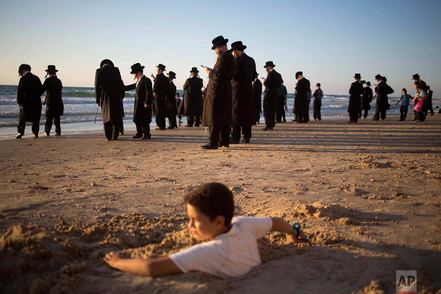  A boy is covered in sand as ultra-Orthodox Jewish men of the Vizhnitz Hassidic sect pray on a hill overlooking the Mediterranean Sea as they participate in a Tashlich ceremony, in Herzeliya, Israel, Thursday, Sept. 28, 2017. (AP Photo/Ariel Schalit)