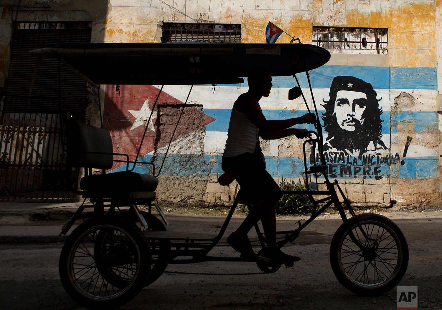  A bicycle taxi rides past a building painted with a Cuban flag and an image of Che Guevara, along with the Spanish slogan "Always toward victory!" in Havana, Cuba, Saturday, March 19, 2016. (AP Photo/Rebecca Blackwell) 