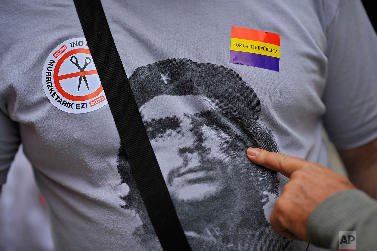 A citizen points to a portrait of ''Che Guevara'' on a shirt of one demonstrator between two stickers, at a protest against the Spanish government's cutback plans, and for a new Spanish Republic, right, in Pamplona, northern Spain, Sunday, Oct. 7, 2