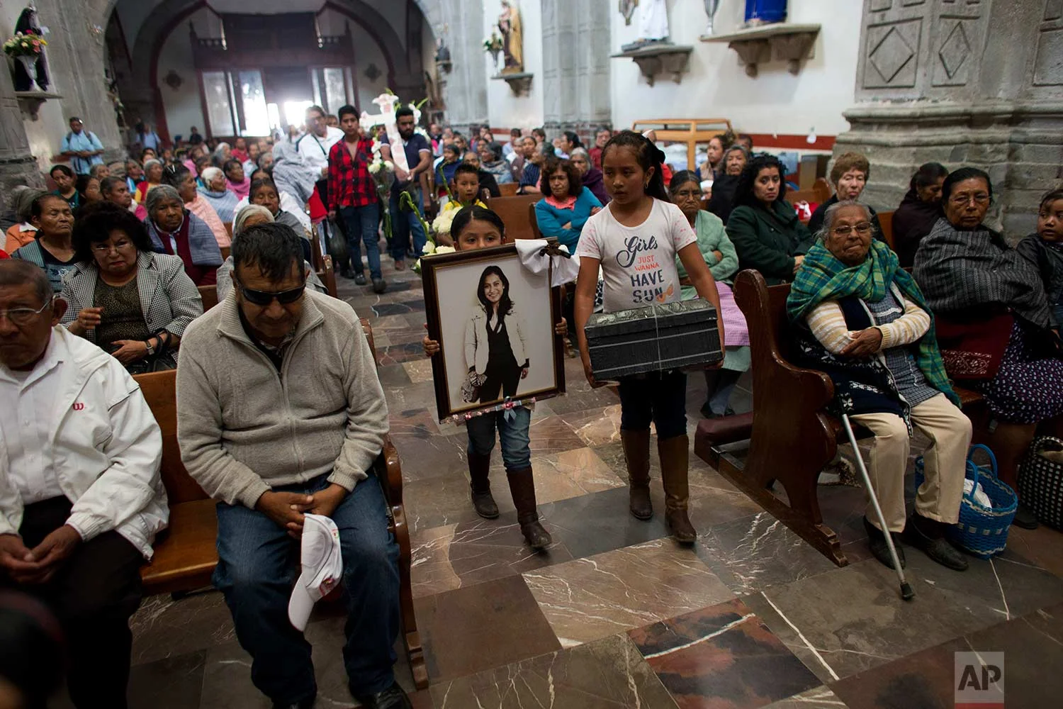In this Aug. 18, 2017 photo, relatives of murdered doctor and mother, Jessica Sevilla Pedraza, carry a framed portrait of her, a cross, and a box of mementos to be buried alongside her grave, as they arrive for Mass in Villa Cuauhtemoc, Mexico state. (AP Photo/Rebecca Blackwell)