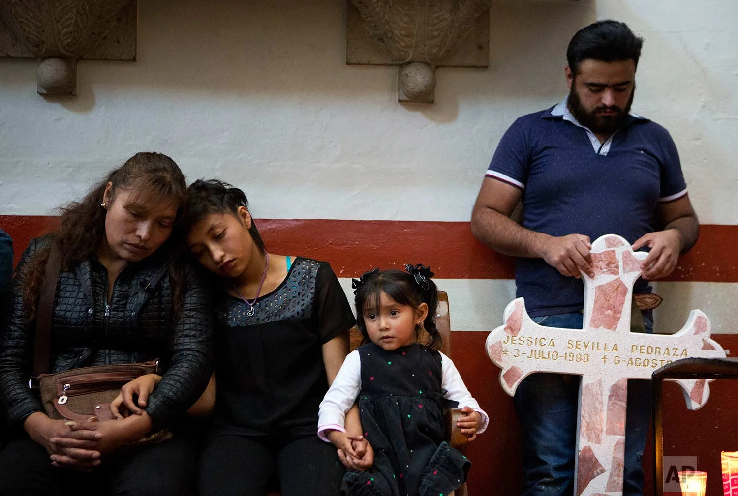 In this Aug. 18, 2017 photo, family members of slain Dr. Jessica Sevilla Pedraza attend a church service, holding a cross for her grave which they brought to be blessed with holy water, in Villa Cuauhtemoc, Mexico state. (AP Photo/Rebecca Blackwell)