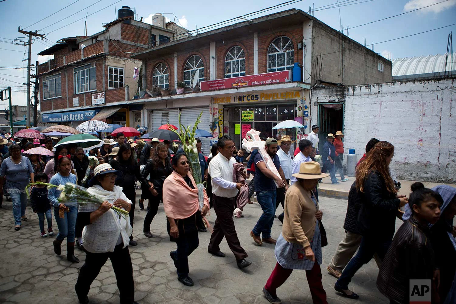 In this Aug. 18, 2017 photo, family and friends walk in procession from the church to the cemetery carrying a cross anointed with holy water to mark the grave of murdered doctor and mother Jessica Sevilla Pedraza, 29, in Villa Cuauhtemoc, Mexico state. (AP Photo/Rebecca Blackwell)