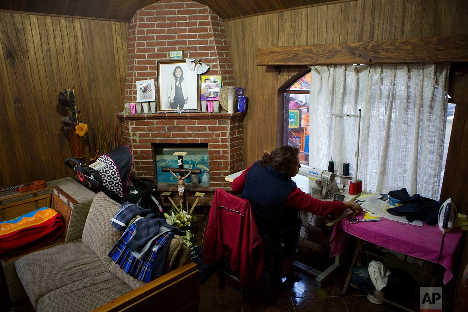 In this Aug. 23, 2017 photo, Juana Pedraza sits next to a small altar in honor of her oldest daughter Jessica, who was murdered at age 29, as she sews school uniforms to order at her home in Villa Cuauhtemoc, Mexico state. (AP Photo/Rebecca Blackwell)
