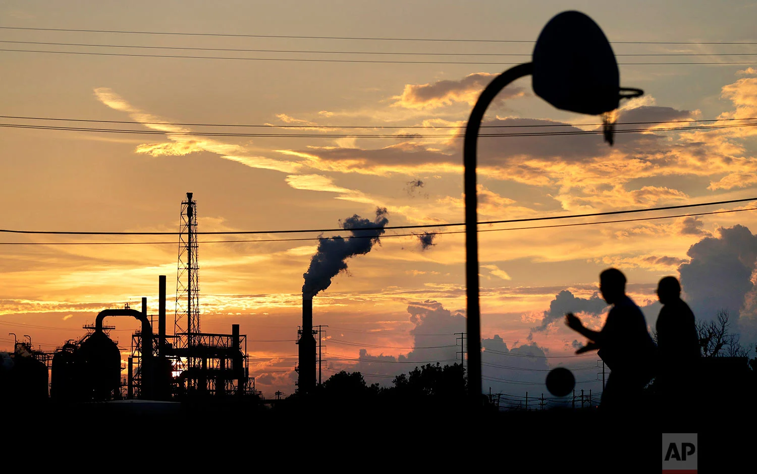 An oil refinery stands in the background as children play on a basketball court in Port Arthur, Texas, Wednesday, Sept. 27, 2017. The region's economy is tied to the petroleum industry more than in any other place in America: the concentration of people here employed by refineries is 81 times higher than the rest of the country. (AP Photo/David Goldman)