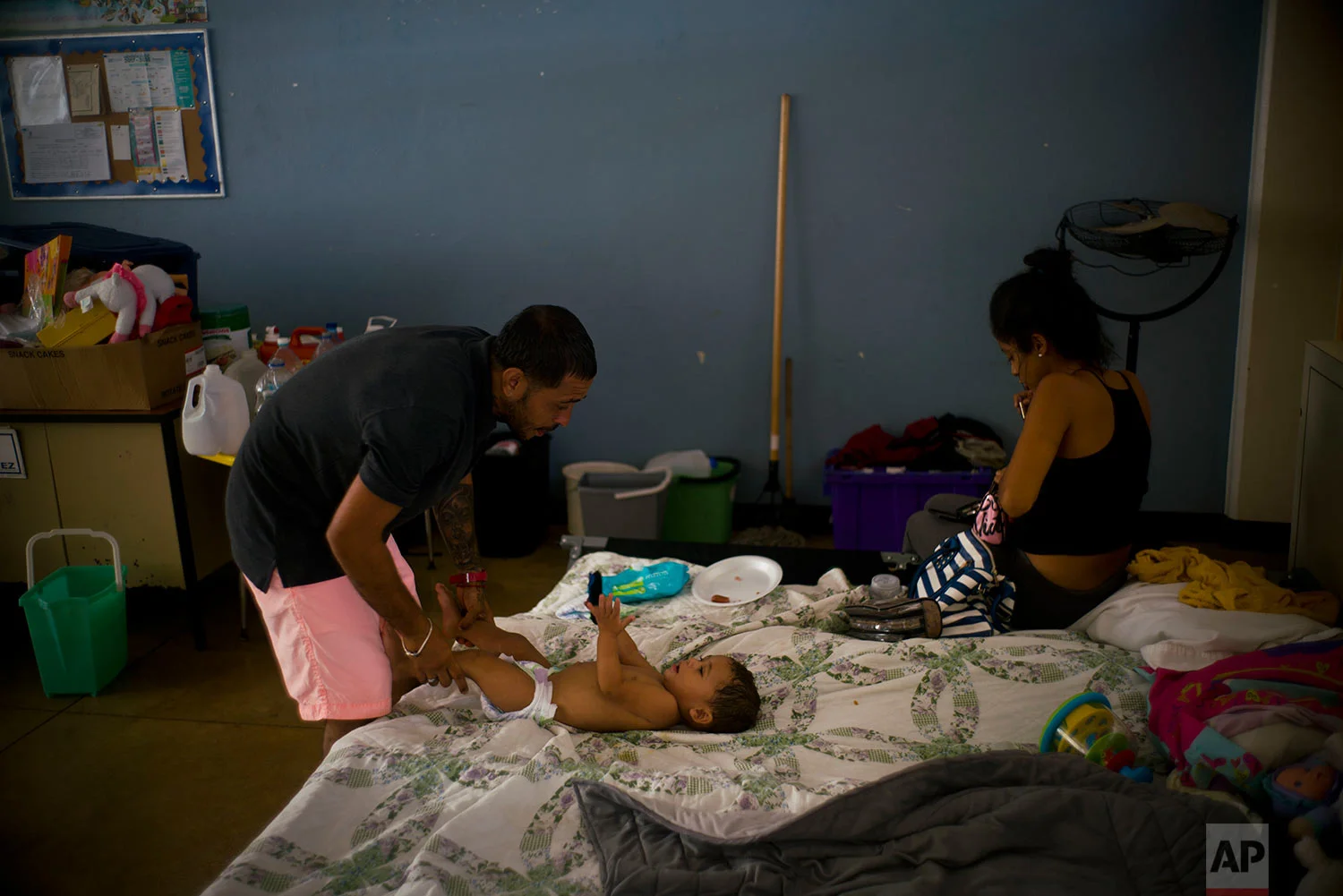 In this Friday, Oct. 13, 2017 photo, Arden Dragoni changes his baby's diaper as his wife Sindy puts on her makeup on their bed inside a classroom at a school serving as a shelter for people left homeless by Hurricane Maria in Toa Baja, Puerto Rico. (AP Photo/Ramon Espinosa) 