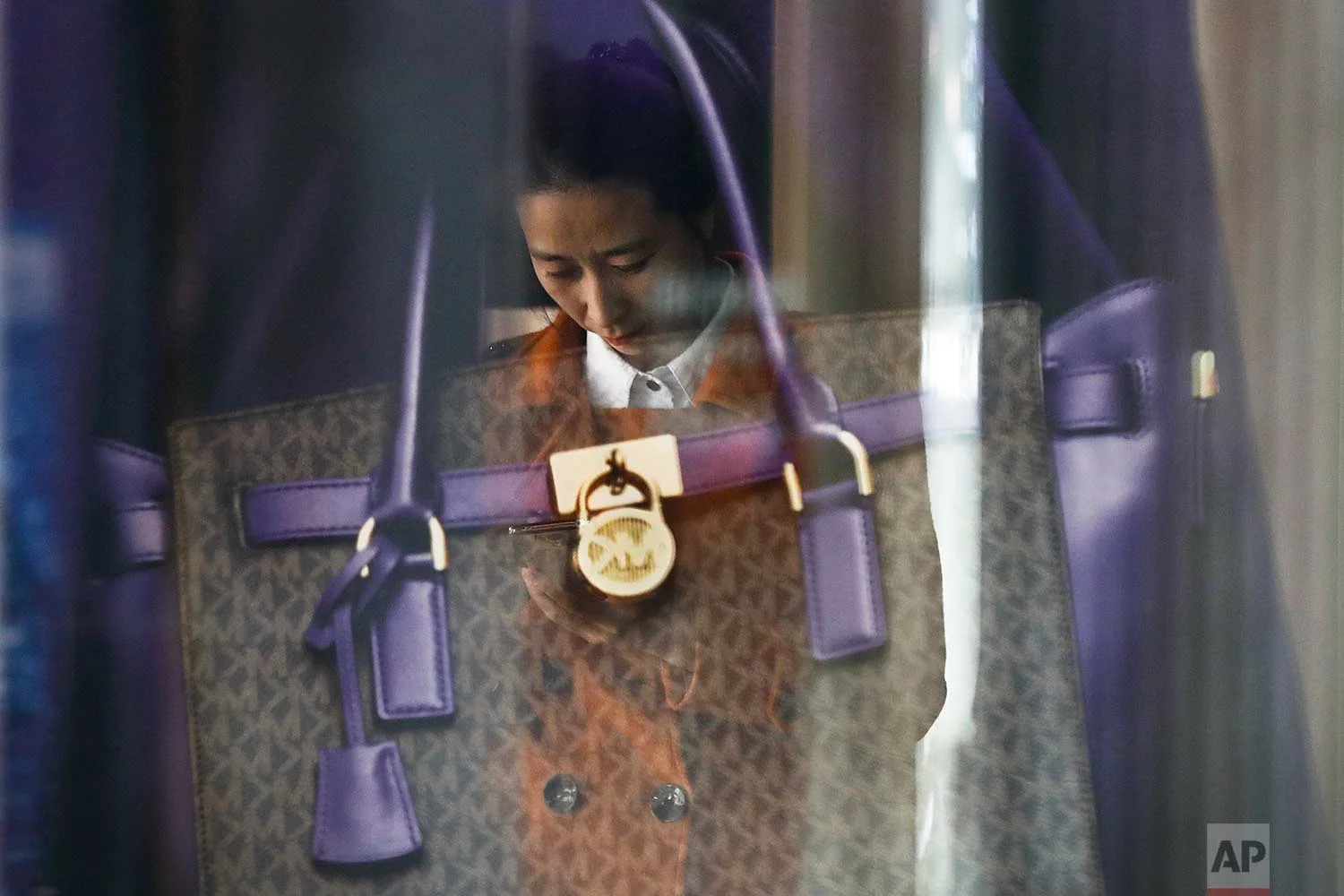 A luxury purse is reflected on a woman checking on her smartphone outside a fashion boutique at a popular shopping mall in Beijing, on Thursday, Oct. 19, 2017. (AP Photo/Andy Wong)