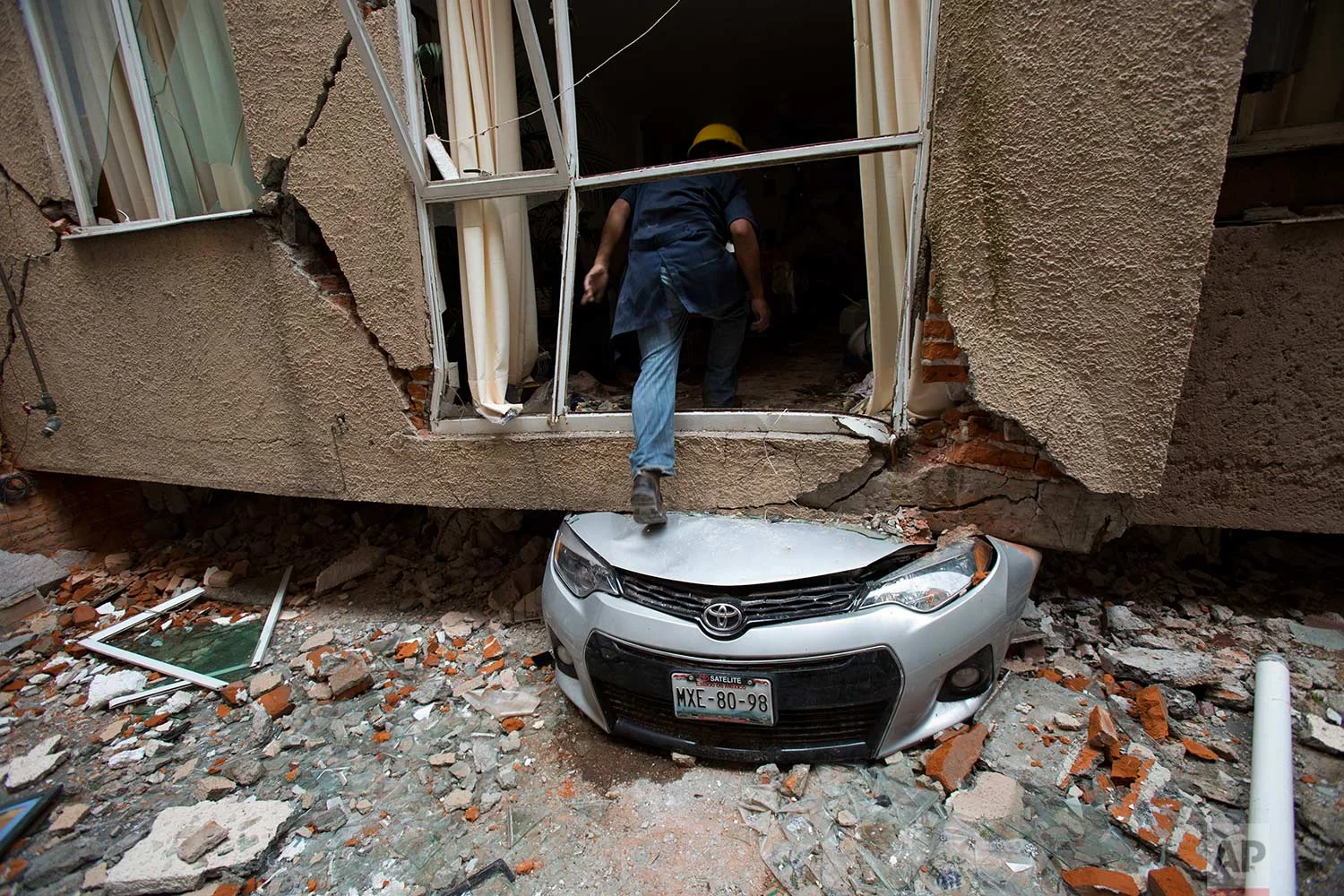 Rodrigo Diaz Mejia climbs over a crushed car into what was a second-story apartment felled by an earthquake a month earlier in the Portales Norte neighborhood of Mexico City, Wednesday, Oct. 18, 2017. (AP Photo/Rebecca Blackwell)