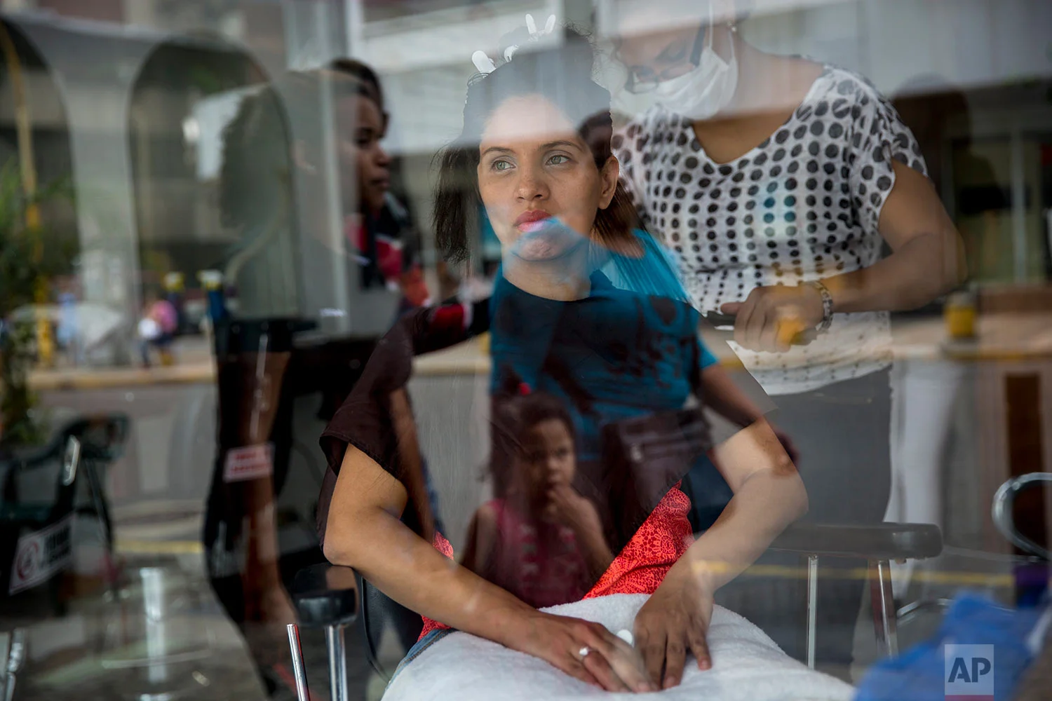 Dayanara Monsalve is seen through a window while waiting for her hairdresser to finish hydrating her hair, in downtown Caracas, Venezuela, Wednesday, Oct. 25, 2017. (AP Photo/Rodrigo Abd)