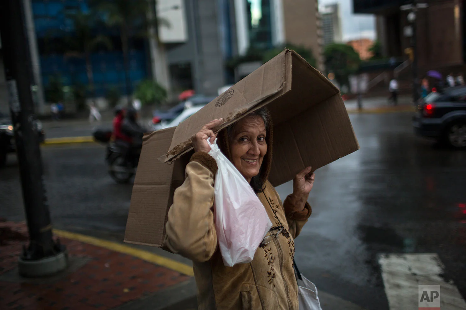 A pedestrian covers herself from the rain with a cardboard box in the financial district of Caracas, Venezuela, Thursday, Oct. 26, 2017. (AP Photo/Rodrigo Abd)