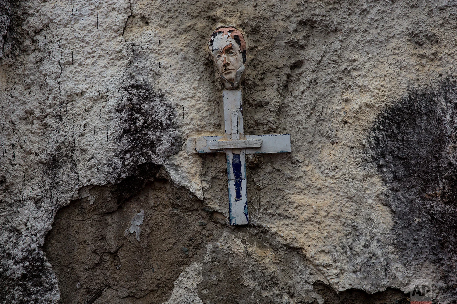 A small mask depicting Venezuela's independence leader Simon Bolivar decorates the top of a cross hanging on a wall along the street in La Vega neighborhood of Caracas, Venezuela, Thursday, Oct. 26, 2017. (AP Photo/Rodrigo Abd)
