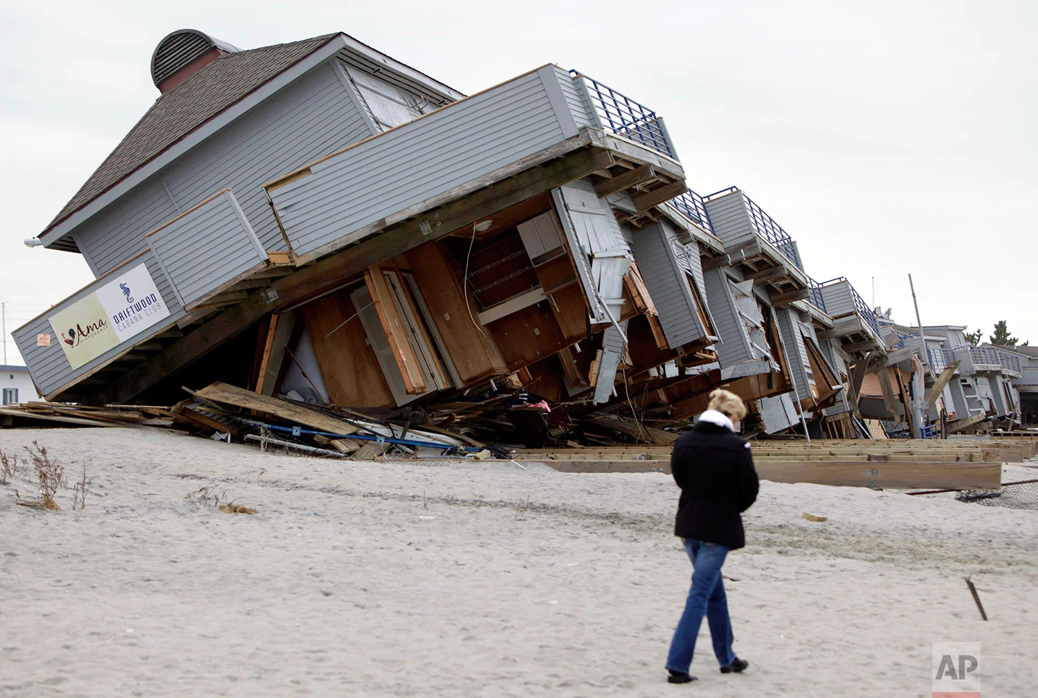A woman walks past a cabana complex on the beach pulled off its foundations by Superstorm Sandy in Sea Bright, N.J., Monday, Nov. 19, 2012. (AP Photo/Seth Wenig)