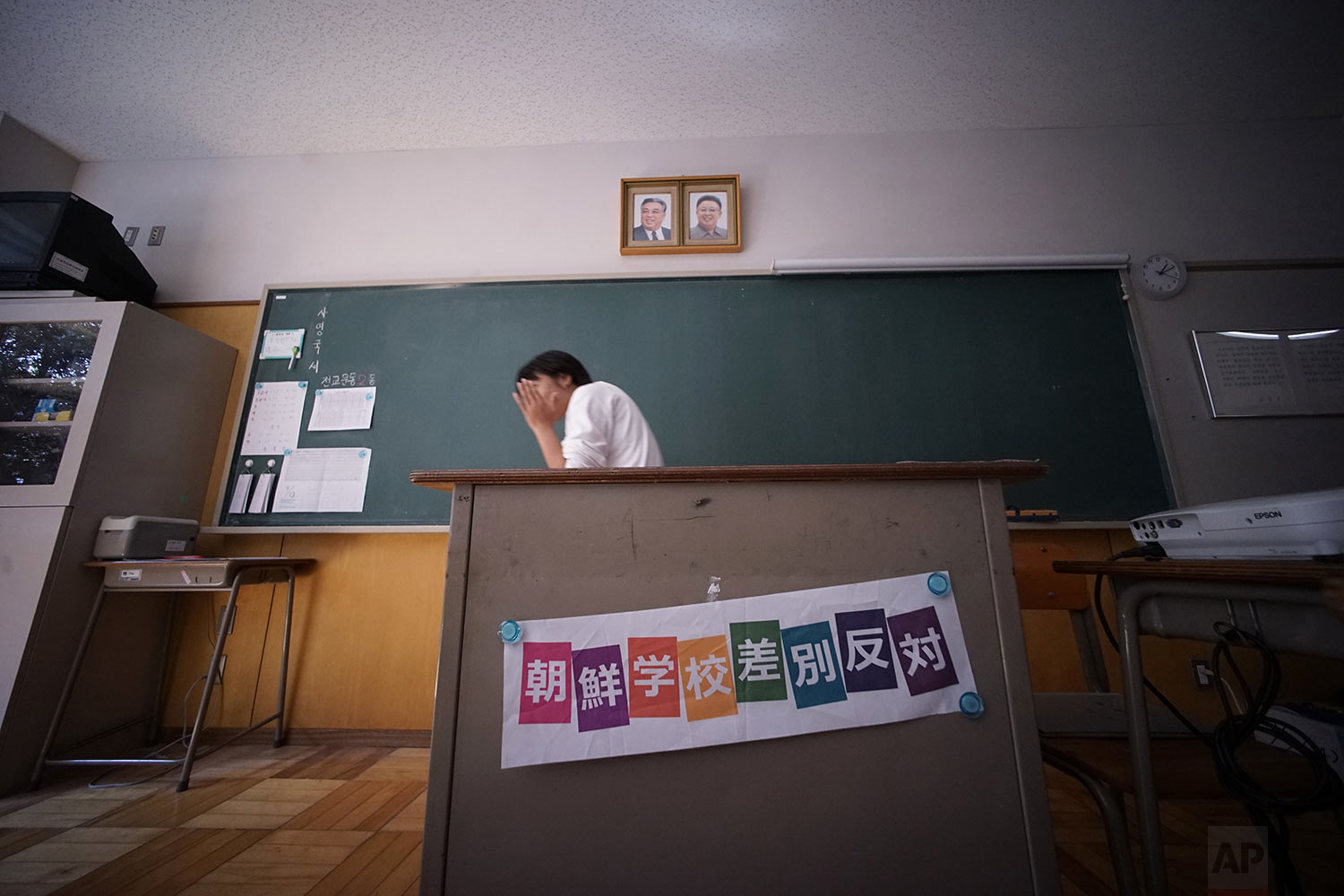  In this Sept. 26, 2017, photo, a student walks below the portraits of the late North Korean leaders Kim Il Sung and Kim Jong Il hang on the wall in a classroom with a banner reading "Against the discrimination against North Korean School" at a Korea