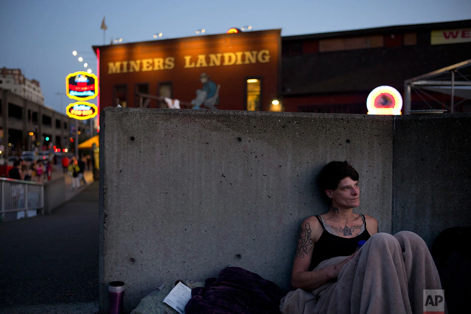 Covering herself with a blanket, homeless woman Christian McKenzie, a 29-year-old heroin addict and mother of a 7-year-old boy, settles down next to a wall in the Waterfront Park area in Seattle on Thursday, Sept. 28, 2017. "I'm doing drugs still, but I'm not doing them as much. I've restrained myself all day not to," said McKenzie. "I miss my kitchen. I miss my kid." (AP Photo/Jae C. Hong)