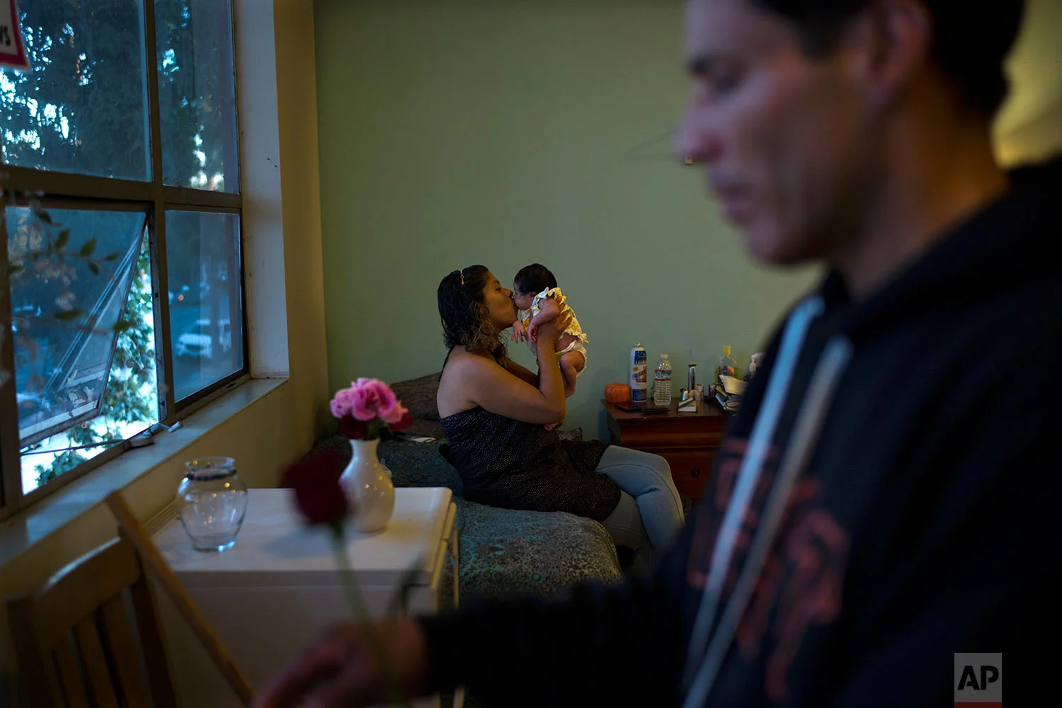 Sitting on a bed in a temporary shelter at Grace Baptist Church on Tuesday, Oct. 24, 2017, Bernadette Ortiz, a 39-year-old homeless woman, kisses her 9-day-old baby girl, Serenity, as her fiance and the baby's father, Ricardo Lopez, foreground, trims flowers they received as gifts after Ortiz gave a birth, in San Jose, Calif. The couple is moving into a studio apartment in a week, Ortiz's first home in five years. (AP Photo/Jae C. Hong)