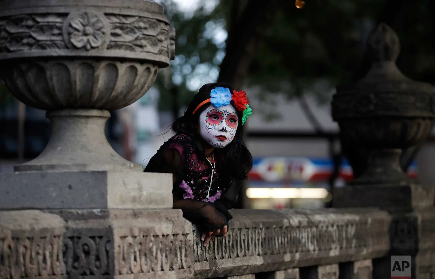 A girl dressed as Mexico's iconic "Catrina" leans against stone benches as she awaits the start of the Grand Procession of the Catrinas, part of upcoming Day of the Dead celebrations in Mexico City, Sunday, Oct. 22, 2017. (AP Photo/Rebecca Blackwell)