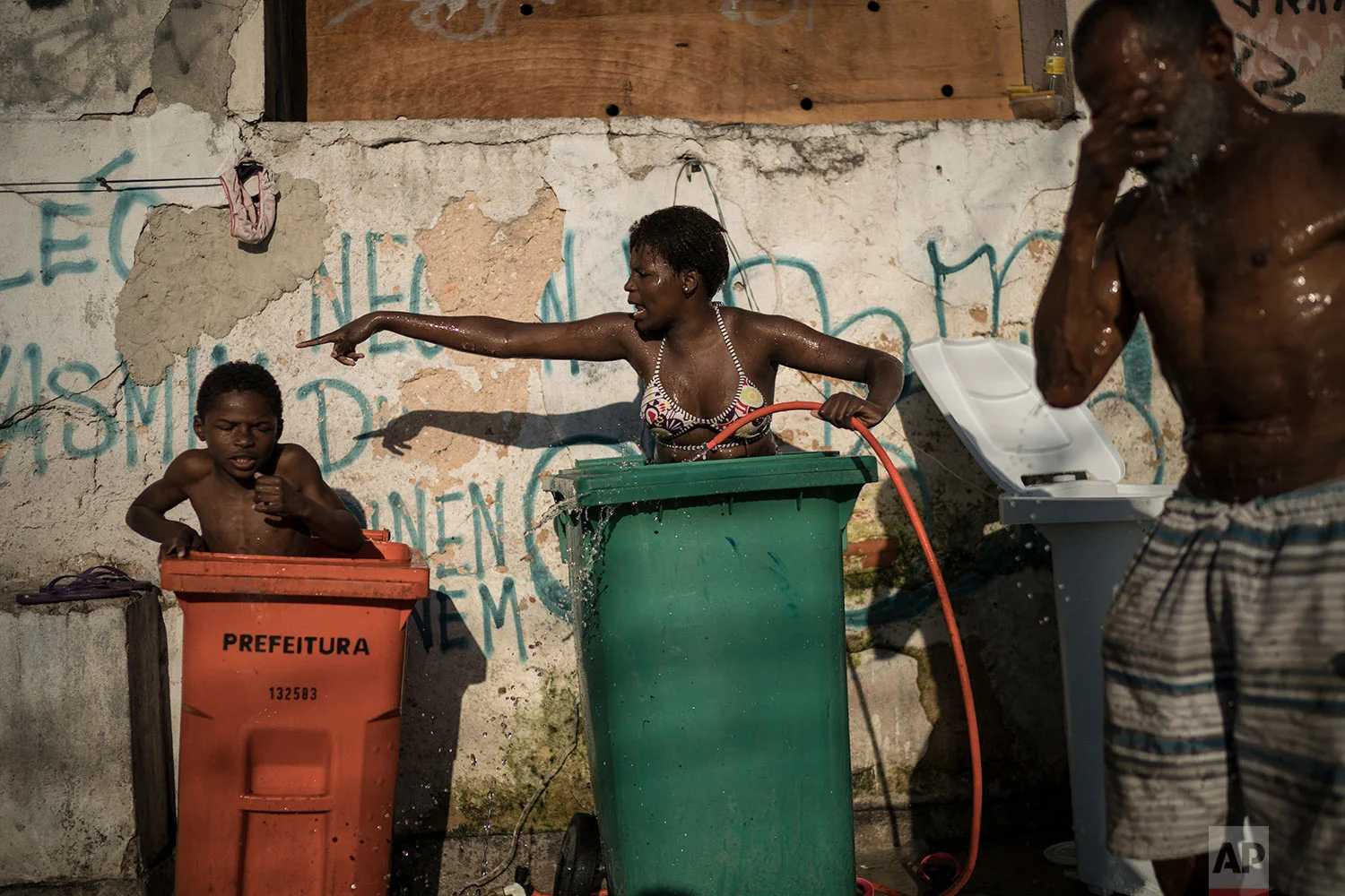 In this Sept. 11, 2017 photo, a woman and youth use tall trash containers to shower outside their squatter building that used to house the Brazilian Institute of Geography and Statistics (IBGE) in the Mangueira slum of Rio de Janeiro, Brazil. The World Bank estimates that between the start of 2016 and the end of this year, 2.5 million to 3.6 million Brazilians will have fallen back below the poverty line of 140 Brazilian reais per month, about $44 at current exchange rates. (AP Photo/Felipe Dana)