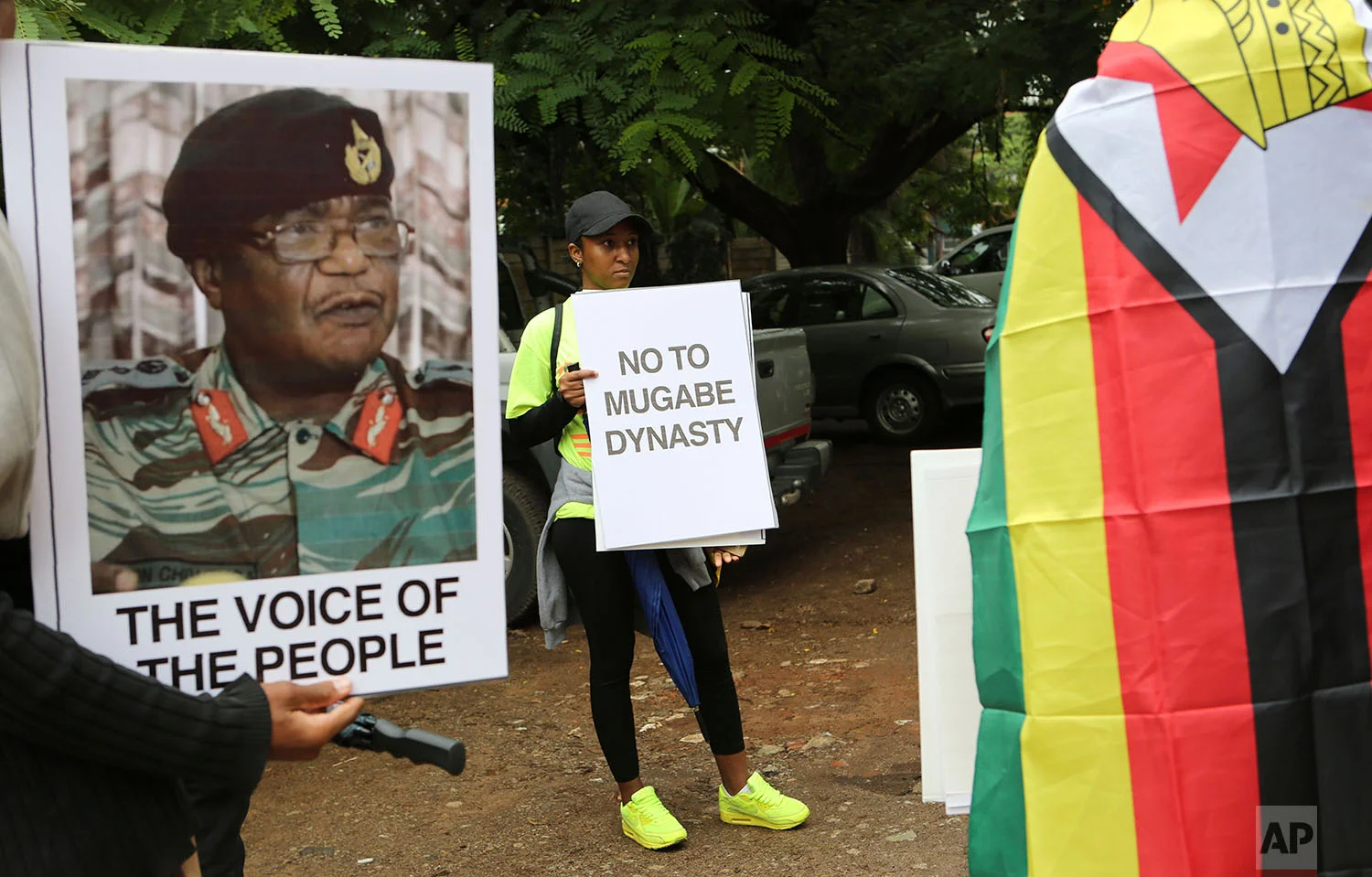 People hold their messages in Harare to demonstrate for the ouster of President Robert Mugabe who is virtually powerless and deserted by most of his allies, Saturday, Nov. 18, 2017. Zimbabwe's generals, including Constantino Chiwenga, on poster left, have placed Mugabe under house arrest and have allowed him limited movement while talks on his exit from office unfold. (AP Photo/Tsvangirayi Mukwazhi)