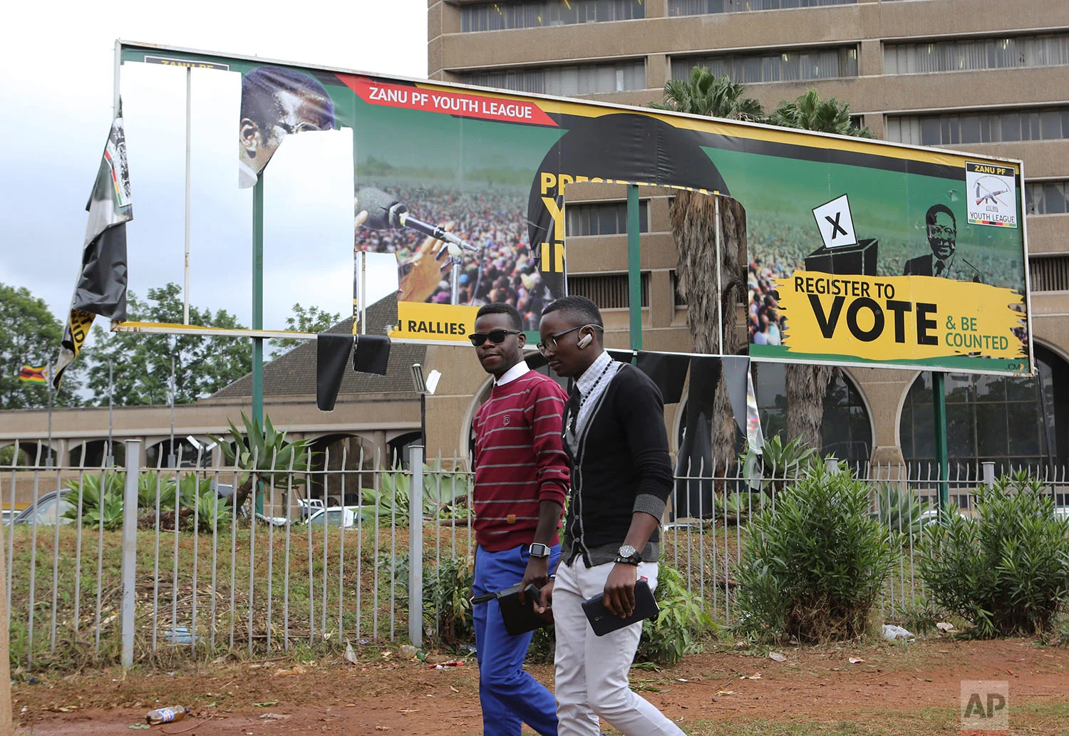 People walk past a partly torn down ruling party banner that showed Zimbabwe President Robert Mugabe's face at the Zanu pf headquarters in Harare, Zimbabwe Sunday Nov. 19, 2017. Clinging to his now virtually powerless post, longtime President Mugabe on Sunday was set to discuss his expected exit with the army commander who put him under house arrest, while the ruling party prepared to recall the world's oldest head of state as its leader. (AP Photo/Tsvangirayi Mukwazhi)