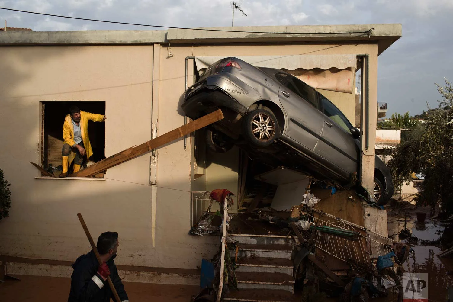 In this Thursday, Nov. 16, 2017 photo, workers try to remove a vehicle wedged into the entrance of a home in the town of Mandra western Athens. A major flash flooding on Wednesday that left at least 21 people dead, turned streets into torrents of mud and debris that swept away cars, collapsed walls and submerged parts of a major highway. (AP Photo/Petros Giannakouris)