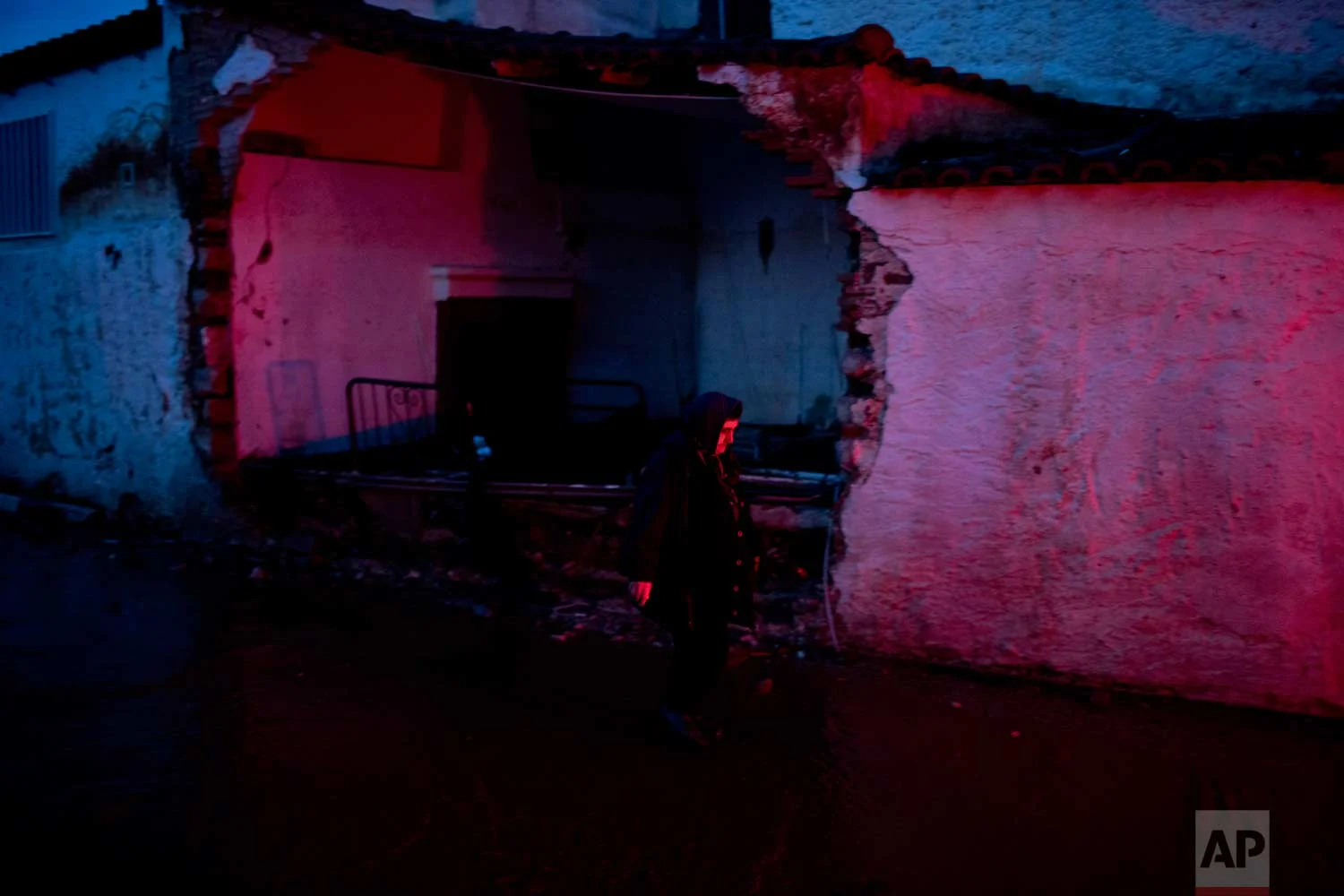 In this Friday, Nov. 17, 2017 photo, an elderly woman walks in front of a flood-damaged house in the town of Mandra western Athens, on Friday , Nov. 17, 2017. (AP Photo/Petros Giannakouris)