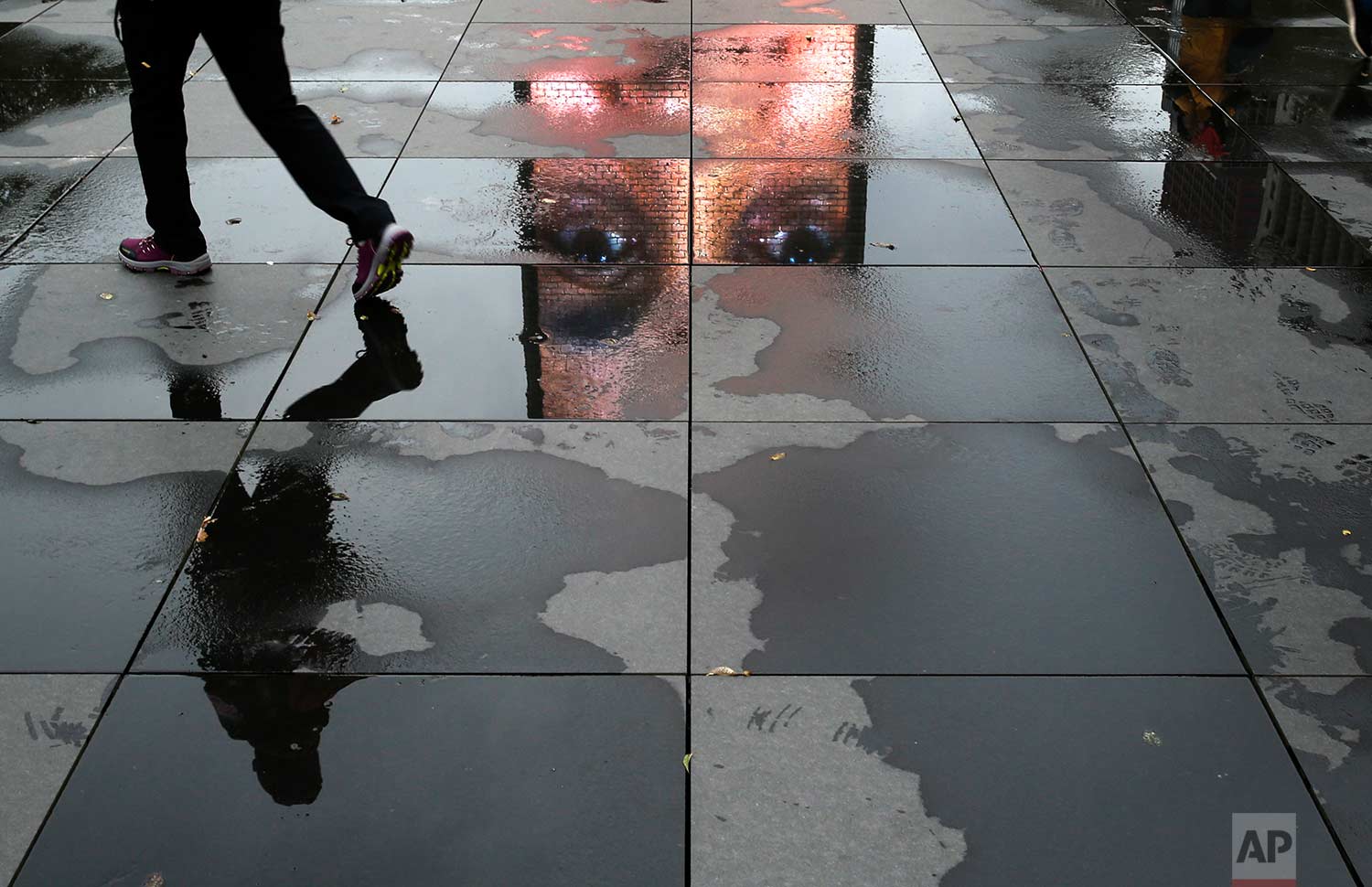 A pedestrian walks through puddles reflecting a projected face displayed on a video sculpture at the Crown Fountain in Chicago's Millennium Park, Tuesday, Nov. 21, 2017, in Chicago. (AP Photo/Charles Rex Arbogast)
