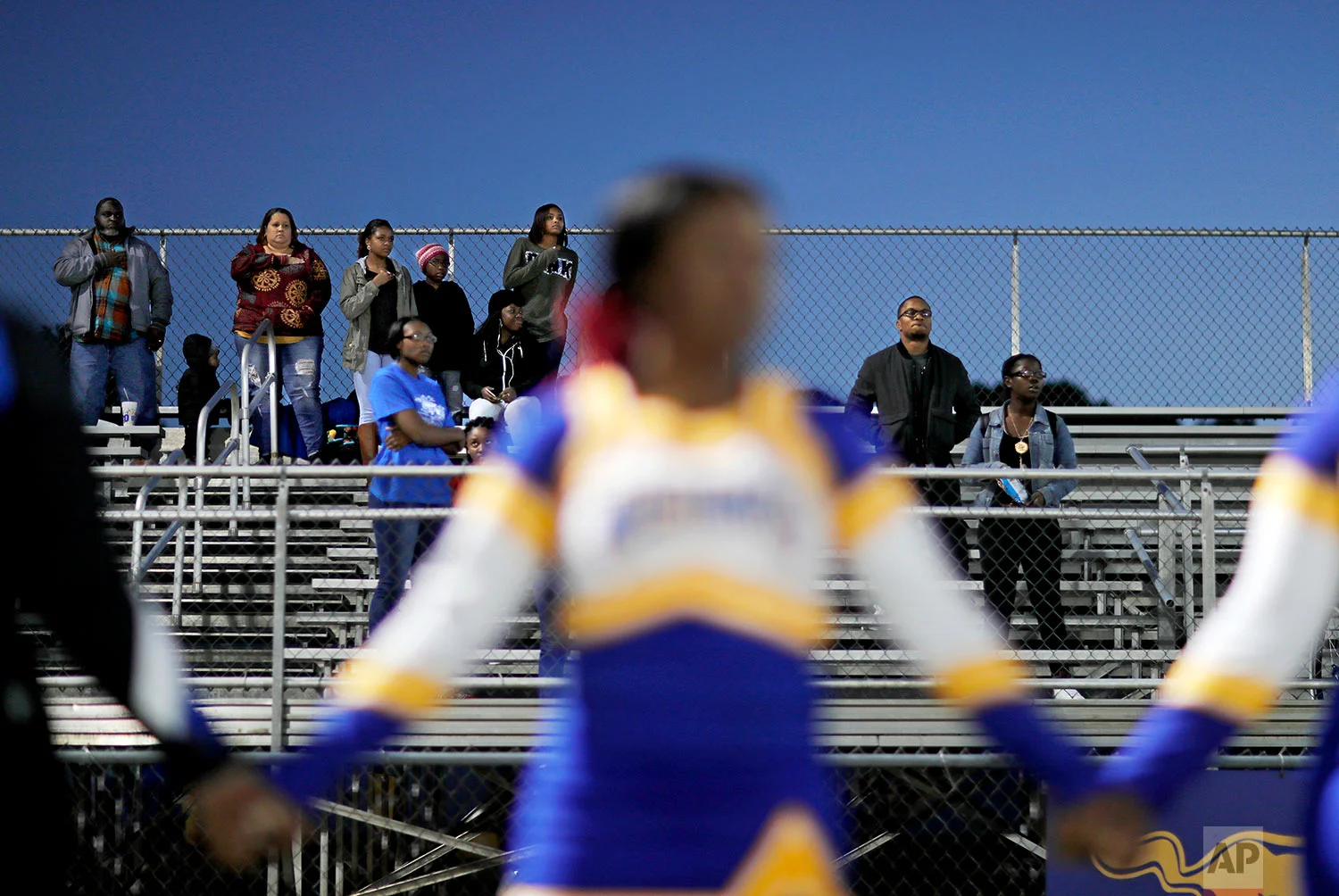 Spectators stand for the national anthem before a South Robeson High School football game in Rowland, N.C., Friday, Oct. 27, 2017. When the cheerleading squad knelt during the national anthem at a recent game, the protest of racial injustice highlighted divisions in Robeson County, North Carolina, the most diverse rural county in America, where voters also helped Donald Trump win the county and the White House. (AP Photo/David Goldman)