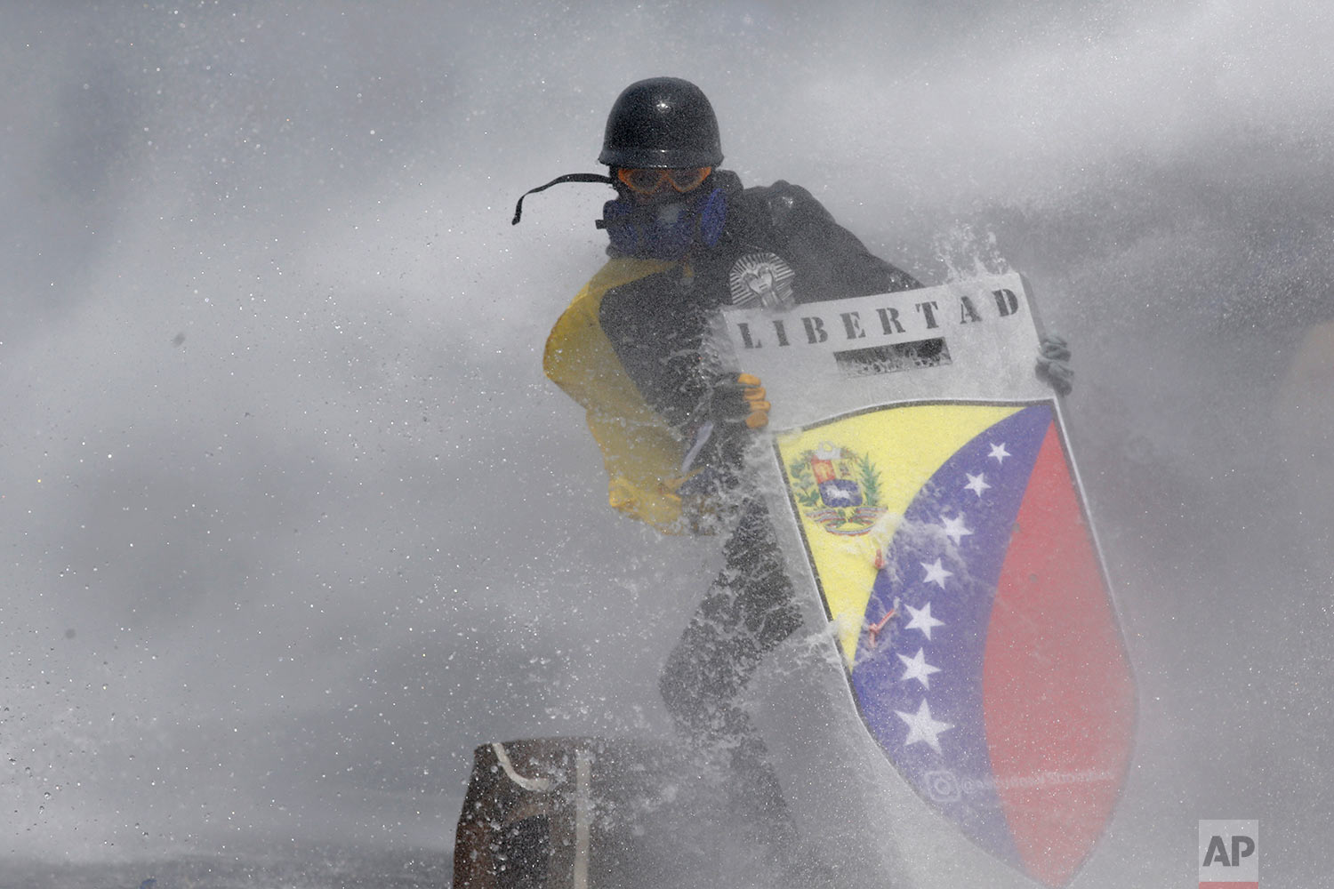 Engulfed in a cloud of tear gas, an anti-government protester protects himself from a jet of water with a shield bearing the Spanish word for "Freedom" during clashes with security forces in Caracas, Venezuela, Wednesday, May 10, 2017. Venezuelan state security forces systematically abused opposition protesters detained during months of deadly political unrest earlier this year, Human Rights Watch charged. (AP Photo/Ariana Cubillos, File)