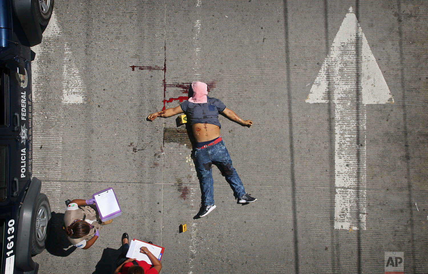 Federal police investigators take notes by the body of a man shot in broad daylight on a central avenue in Acapulco, Mexico, Sunday, Aug. 13, 2017. At least four people were shot in this Pacific coast city Sunday, after Mexico had recently recorded its highest monthly murder total in at least 20 years. (AP Photo/Bernandino Hernandez)