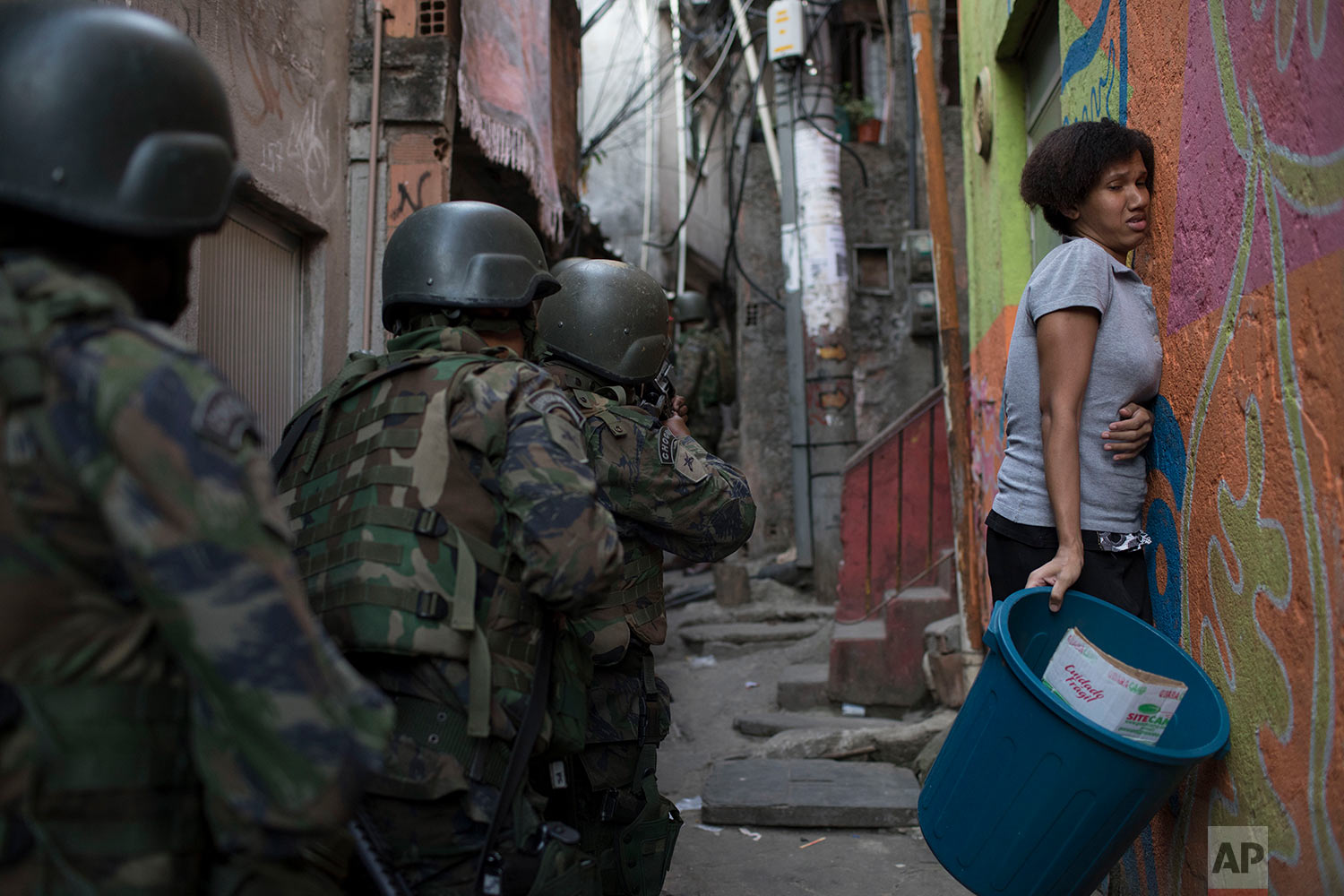 A woman presses herself against the wall as soldiers patrol an alley in Rocinha slum in Rio de Janeiro, Brazil, Friday, Sept. 22, 2017. Shootouts erupted in several areas of Rio de Janeiro on Friday, prompting Brazilian authorities to shut roads, close schools and ask for the army to intervene. (AP Photo/Leo Correa)
