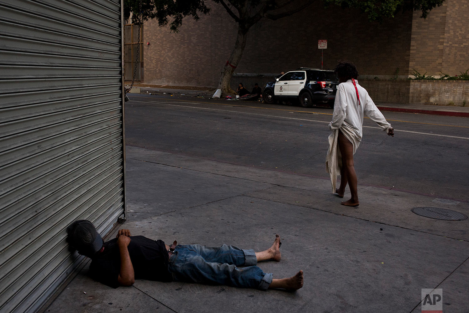 A mentally ill homeless woman walks past a man sleeping on a sidewalk in the Skid Row area of downtown Los Angeles, Friday, Sept. 1, 2017. (AP Photo/Jae C. Hong)