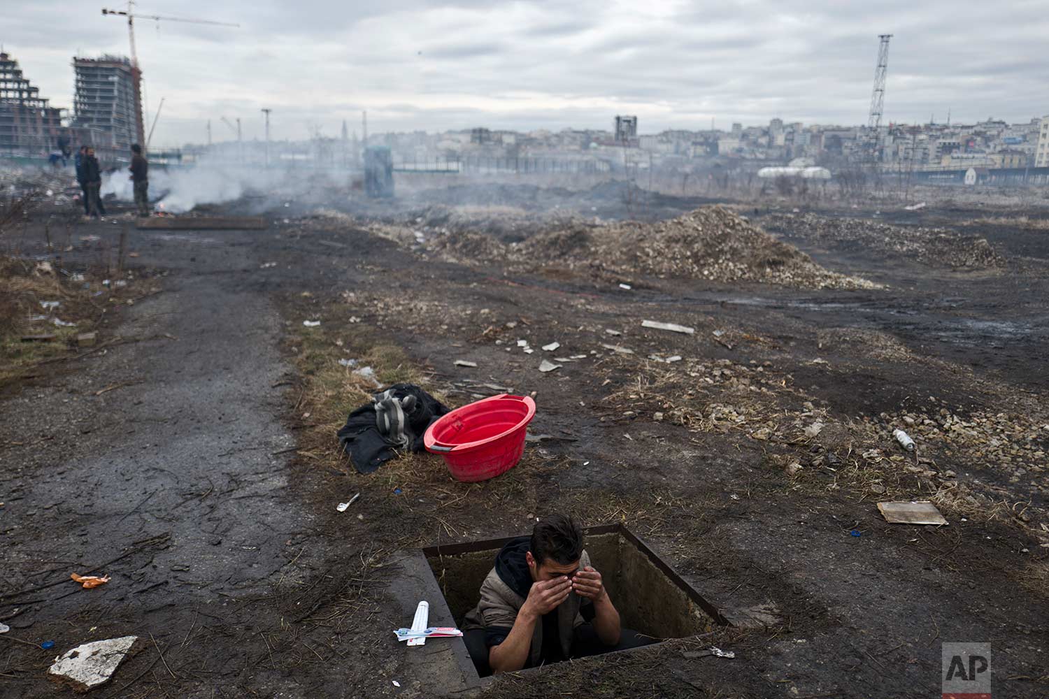  In this Thursday, Feb. 2, 2017 photo, an Afghan refugee youth washes himself in a hole in the ground outside an old train carriage where he and other migrants took refuge in Belgrade, Serbia. Hundreds of migrants have been sleeping rough in freezing