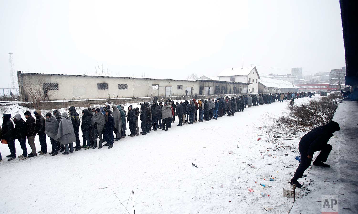  In this Tuesday, Jan. 10, 2017 photo, migrants queue for food in front of an abandoned warehouse in Belgrade, Serbia. Hundreds of migrants are sleeping rough in parks and make-shift shelters in the Serbian capital in freezing temperatures waiting fo