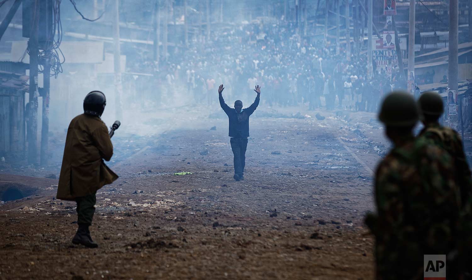  In this Thursday, Aug. 10, 2017 photo, a man seeking safety walks with his hands in the air through a thick cloud of tear gas towards riot police, as they clash with protesters throwing rocks in the Kawangware slum of Nairobi, Kenya. International o