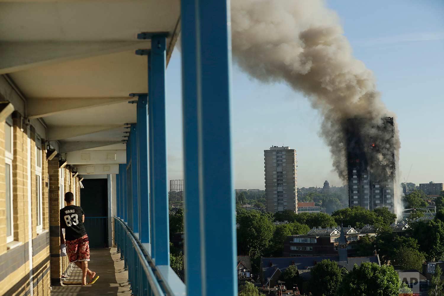  In this Wednesday, June 14, 2017 photo, a resident in a nearby high-rise building watches smoke rise from a massive fire at the high-rise Grenfell Tower in London. (AP Photo/Matt Dunham) 
