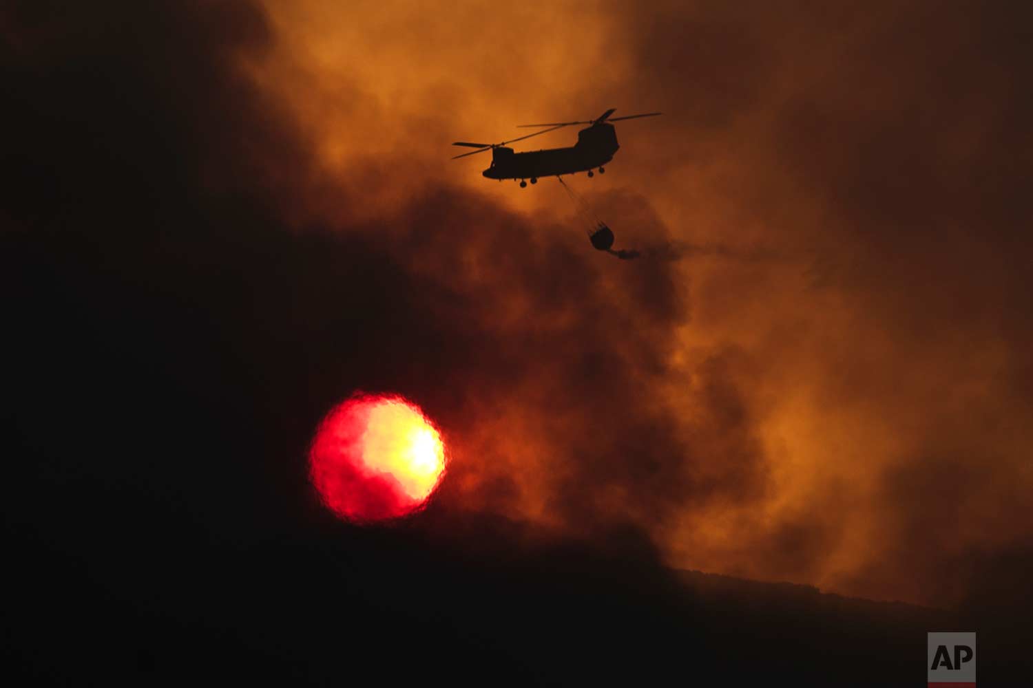  In this Tuesday Aug. 15, 2017 photo, a fire fighting helicopter flies amid smoke as the sun sets during a forest fire near Kapandriti  north of Athens. A large wildfire north of Athens is threatening homes as it sweeps through pine forest for a thir