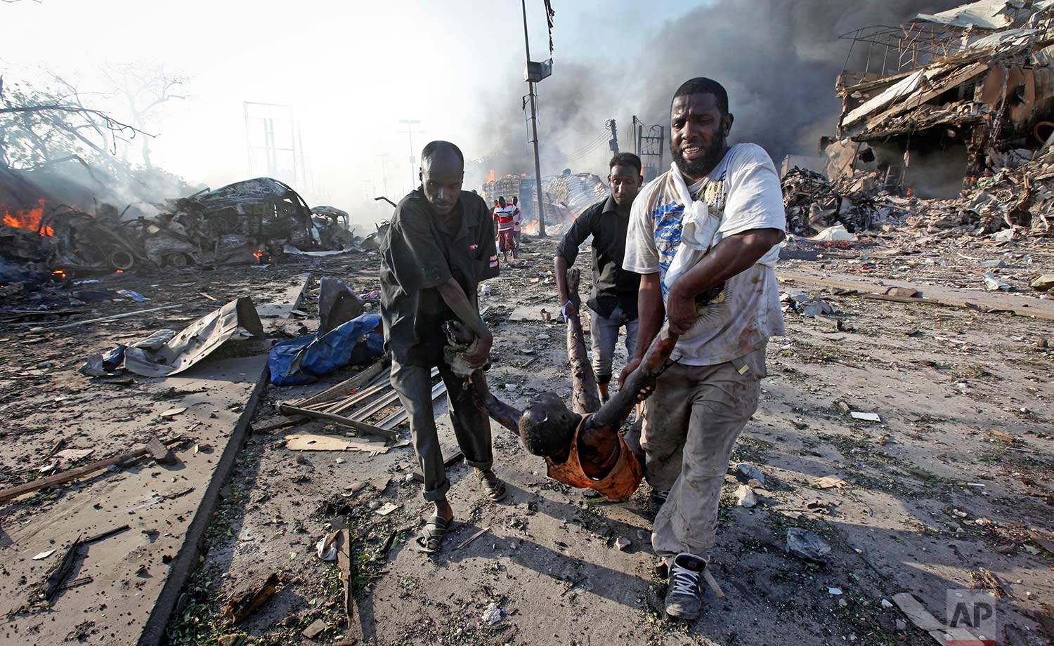  In this Saturday, Oct. 14, 2017 photo, Somalis remove the body of a man killed in a blast in the capital Mogadishu, Somalia. A huge explosion from a truck bomb has killed at least 20 people in Somalia's capital, police said Saturday, as shaken resid