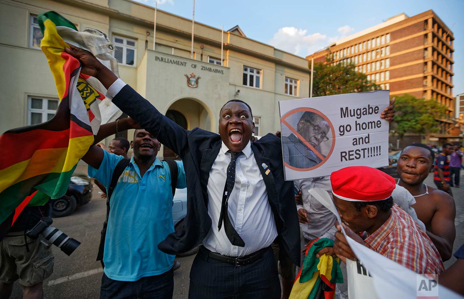  In this Tuesday, Nov. 21, 2017 photo, Zimbabweans celebrate outside the parliament building immediately after hearing the news that President Robert Mugabe had resigned, in downtown Harare, Zimbabwe. Mugabe resigned as president with immediate effec