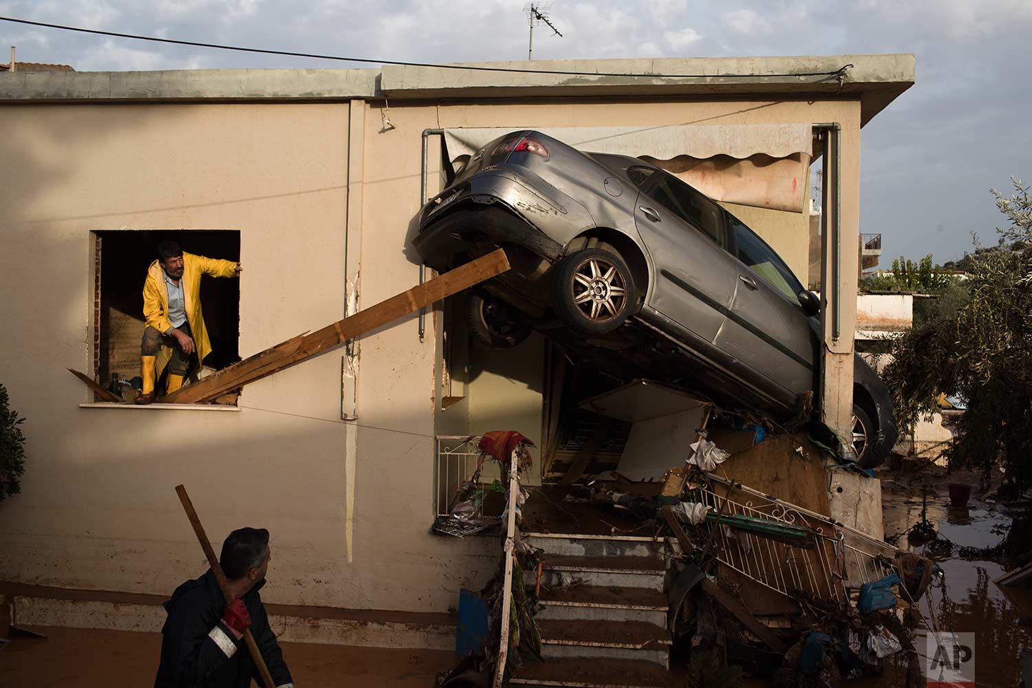  In this Thursday, Nov. 16, 2017 photo, workers try to remove a vehicle wedged into the entrance of a home in the town of Mandra western Athens. A major flash flooding on Wednesday that left at least 21 people dead, turned streets into torrents of mu