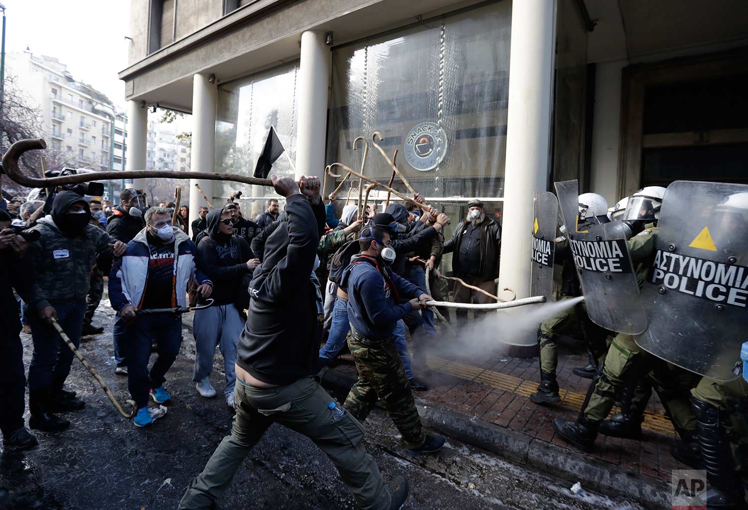  In this Wednesday, March 8, 2017 photo, riot police clash with protesting farmers outside the greek Agriculture Ministry, in Athens. Police fired tear gas to prevent farmers from forcing their way into the ministry building, while protesters respond