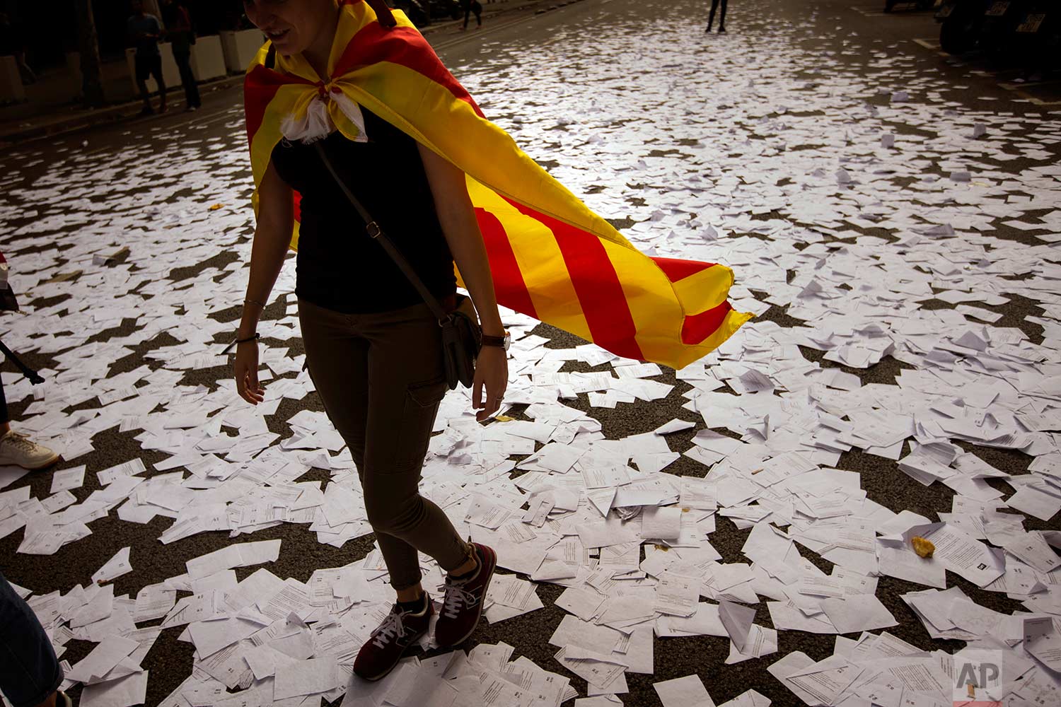  In this Tuesday Oct. 3, 2017 photo, a woman wearing an estelada or independence flag walks a long a street covered with referendum ballots threw by pro-independence demonstrators, during a rally in front of the Spanish Partido Popular ruling party h