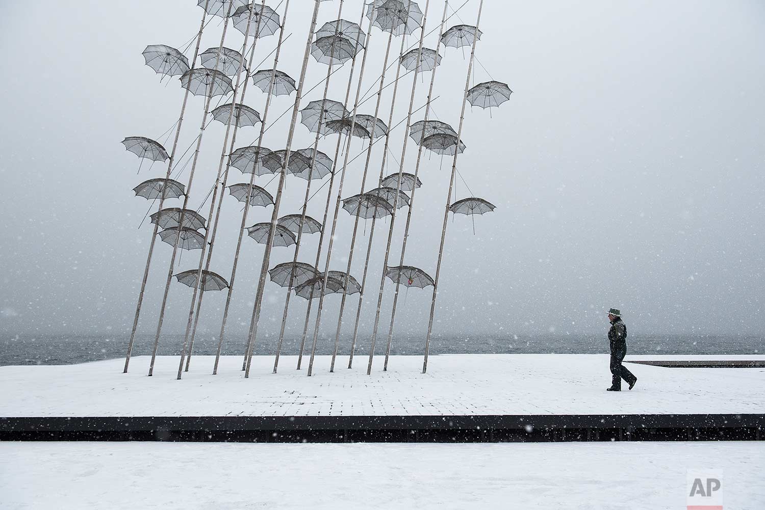  In this Tuesday, Jan. 10, 2017 photo, a woman walks past "Umbrellas" sculpture, by George Zongolopoulos, at the seafront of the northern Greek city of Thessaloniki. Snow closed hundreds of schools in the country, as added pressure on the government 