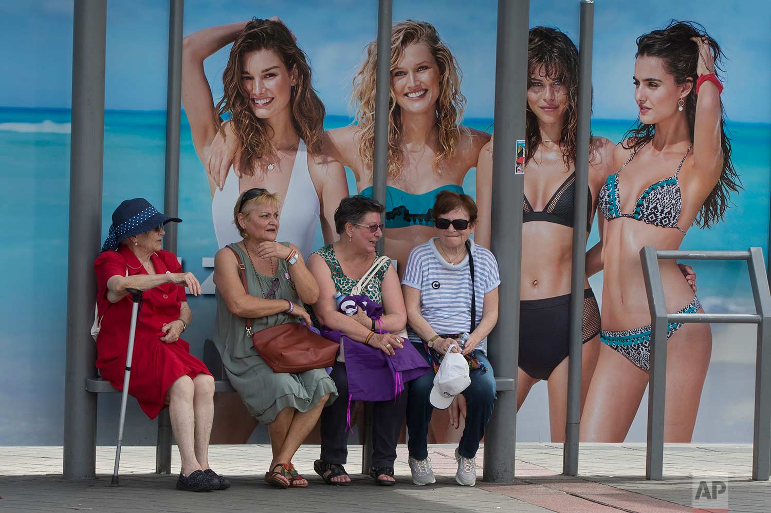  In this Saturday, May 27, 2017 photo, four women wait at a bus stop in front of an advertising poster for swimwear and beach wear in Madrid, Spain. (AP Photo/Paul White) 